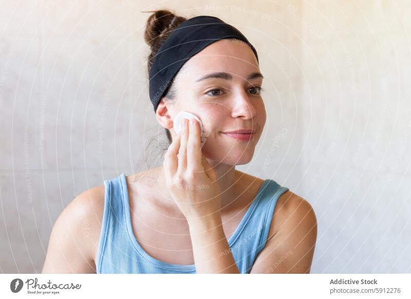 Woman practicing skincare with a cotton pad in a bright bathroom woman routine self-care headband youthful face morning hygiene beauty health wellness daily