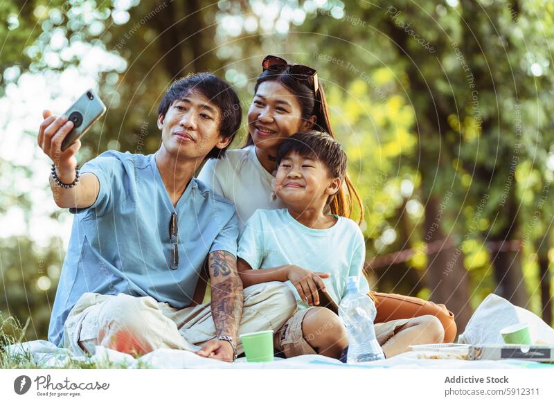 Asian family enjoying a sunny picnic with a selfie moment asian summer park outdoor cheerful happiness recreation leisure bonding smartphone photography nature