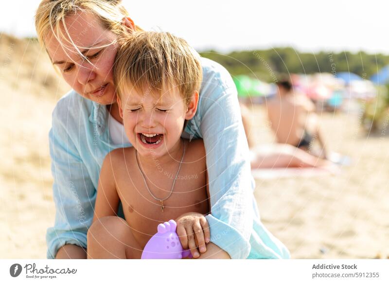 Mother comforts son during beach day in Italy italy mother crying sea summer sand unhappiness family vacation travel sunny child woman splashing unhappy