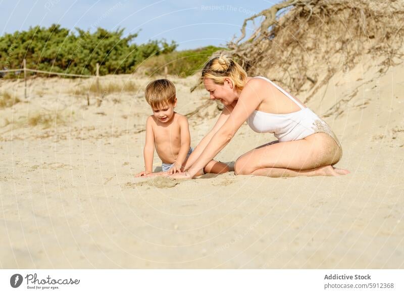 Mother and young son enjoying time together on a sandy beach mother play family child woman summer vacation holiday italy dune vegetation sunny leisure