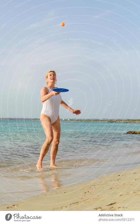 Woman playing with Paddle at the beach woman italian sand sea sky sunny joy swimsuit white blue toss ball orange clear water holiday summer leisure vacation