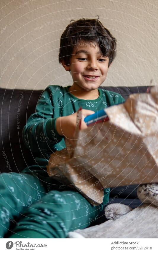 Young boy in festive pajamas excitedly opening a Christmas gift christmas smile joy indoor cozy heartwarming holiday seasonal celebration excitement happy child