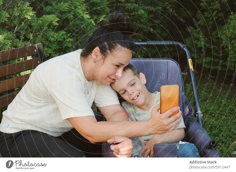 Mother and son enjoy time outside, both smiling and engaging mother cerebral palsy wheelchair smartphone outdoor happy family care support love disability