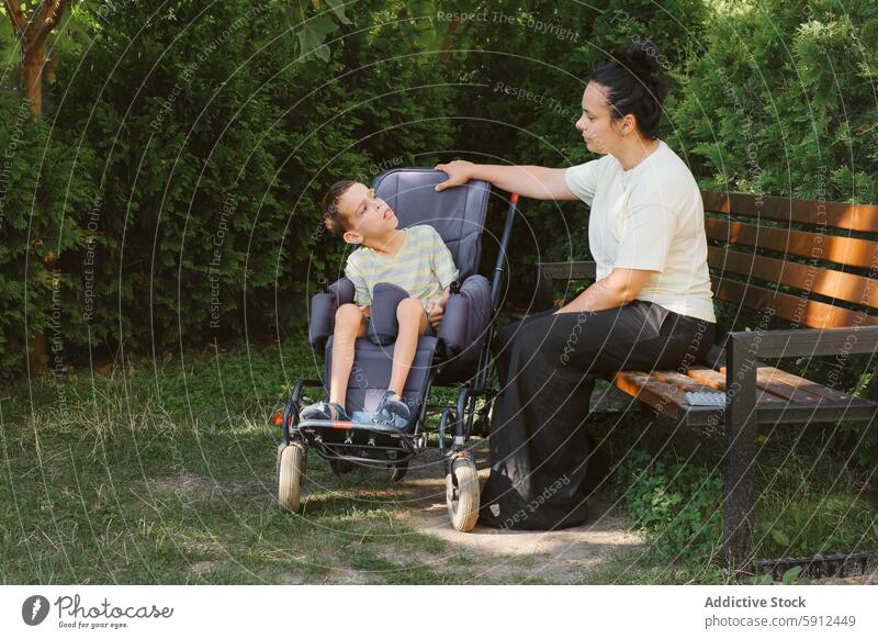 Tender moment between mother and son with cerebral palsy in park wheelchair outdoors care disability love interaction woman boy sitting summer green tree nature