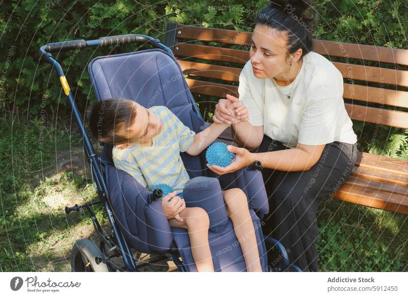 Mother and son with cerebral palsy enjoying time outdoors mother wheelchair park care disability support love tactile interaction bench greenery daytime