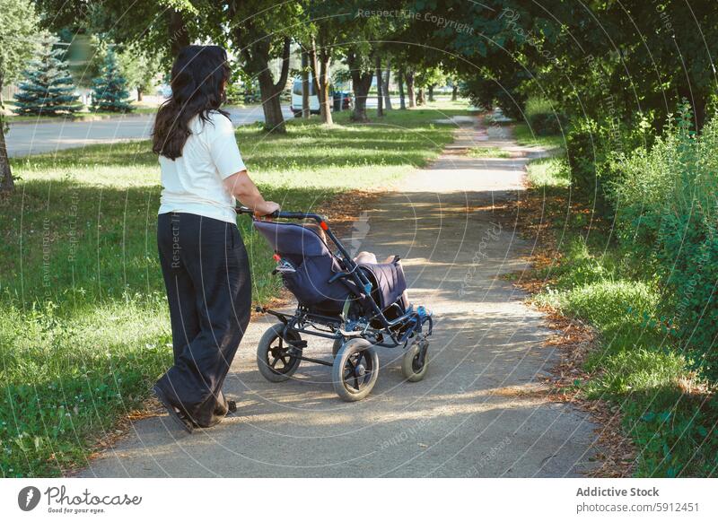 Mother walking with son in wheelchair in park mother cerebral palsy nature pathway unrecognizable anonymous faceless back view tree outdoor caregiving support