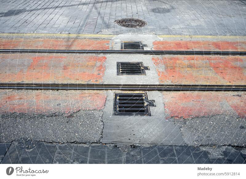 Rails and tracks of the streetcar with manhole cover or manhole cover between old gray and crumbling paving stone in a pedestrian zone in sunshine in Bursa at the Uludag Mountains in Turkey