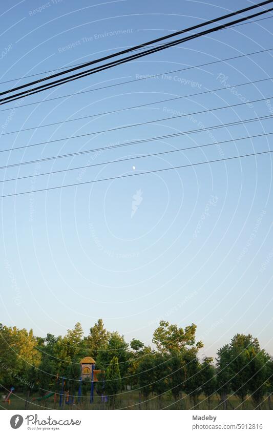 Power line and power lines along the village road against a blue sky in the light of the evening sun with a park and children's playground in the background in the village of Maksudiye near Adapazari in the province of Sakarya in Turkey