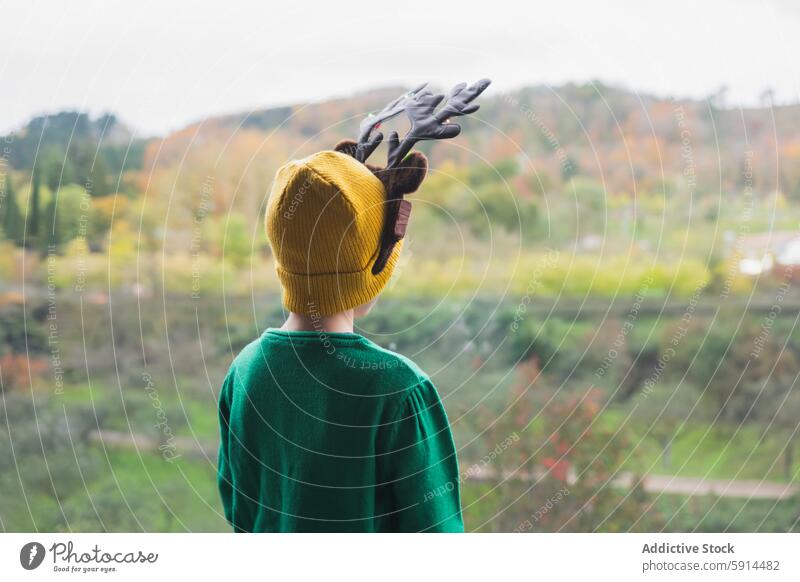 Child with reindeer antlers overlooking autumn landscape child yellow beanie green sweater high vantage point festive christmas outdoor scenic view colorful