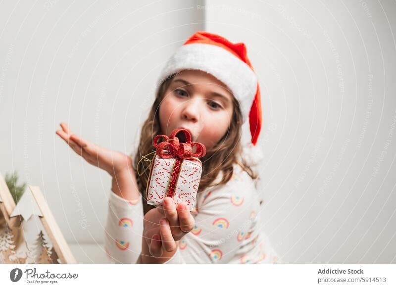 Young girl in Santa hat presenting a small Christmas gift christmas santa hat smile festive holiday celebration joy child cheerful happy season december winter