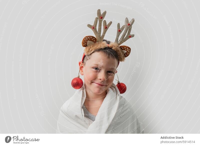 Young boy with reindeer antlers and Christmas baubles christmas holiday winter festive decoration joyful smile white blanket warmth cozy cheerful child kid