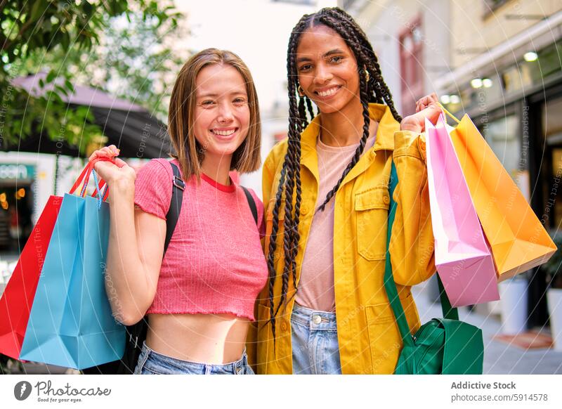 Two happy women shopping together in the city bag urban friend smile joy colorful retail consumer sale purchase casual outdoor street fashion style accessory