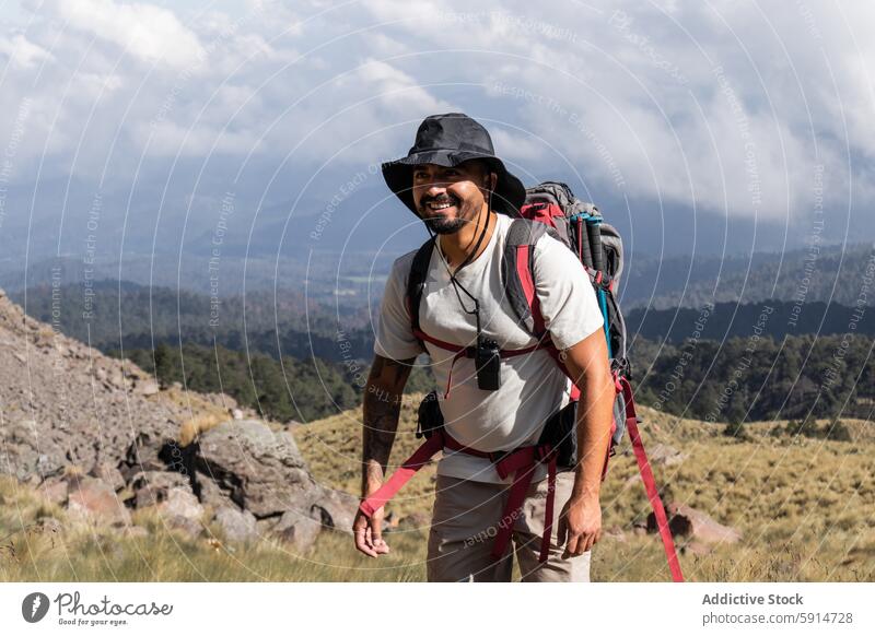 Male hiker smiles while trekking on a dormant volcano male beard tattoo hat backpack trekking pole direct gaze camera rugged terrain outdoor adventure activity