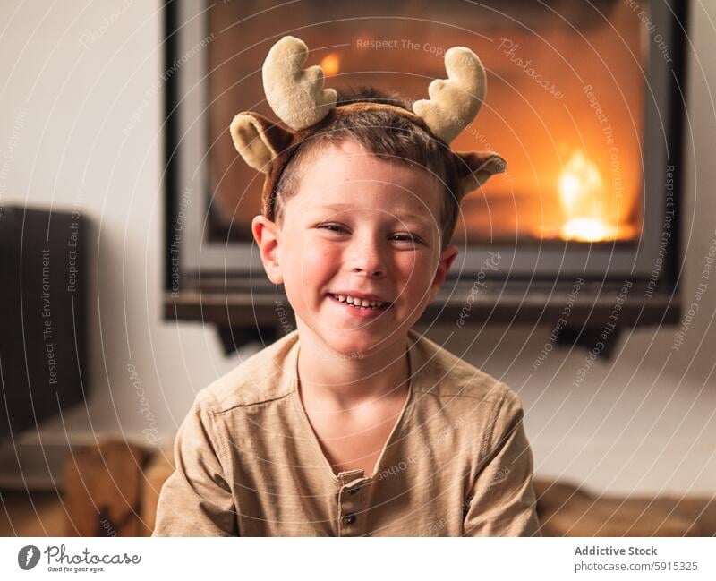 Young boy with reindeer antlers enjoying Christmas christmas child party celebration holiday festive smile joyful home fireplace warmth cozy indoor decoration