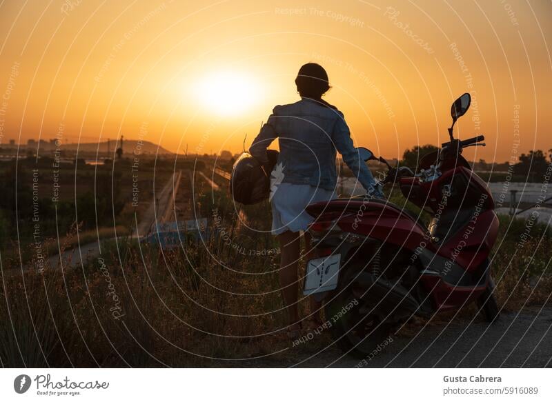 Woman with a helmet and a motorcycle looks at the horizon. Helmet Motorcycle sunrise - dawn Exterior shot Lifestyle travel Silhouette Colour photo