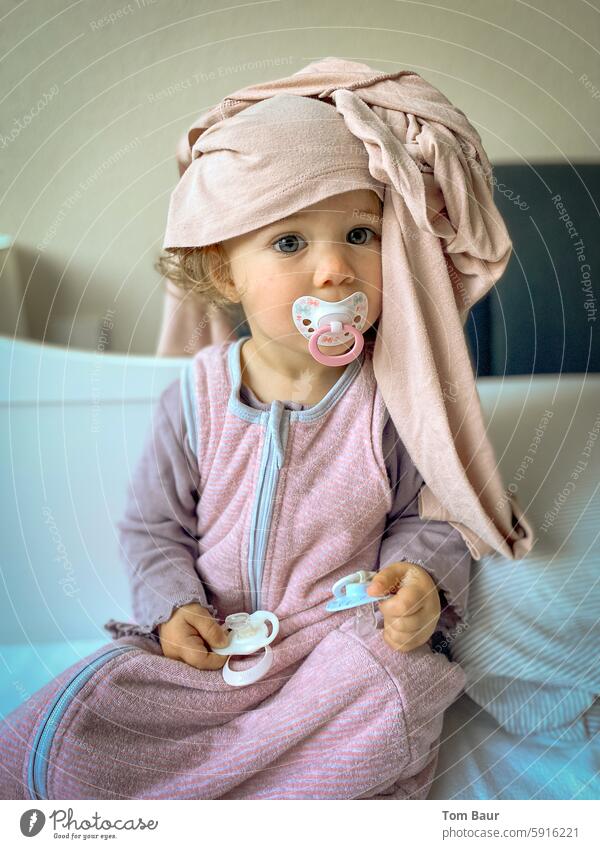 Baby sits in bed with 3 pacifiers and mom's pajamas on her head family bed Soother Looking into the camera Toddler 0 - 12 months Colour photo Face Infancy Cute