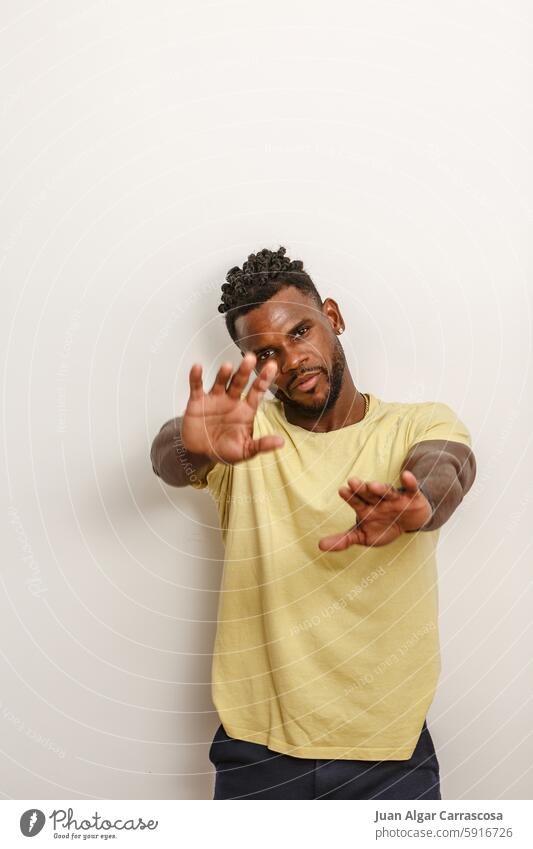 A man poses confidently with outstretched arms against a light backdrop in a casual outfit casual wear yellow t-shirt dark pants playful pose confident stance