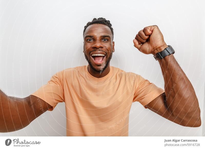 Cheerful man celebrating his success with a broad smile and raised fist in front of a neutral background Man celebration Joy Happiness Success Enthusiasm