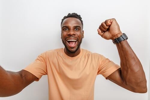 Cheerful man celebrating his success with a broad smile and raised fist in front of a neutral background Man celebration Joy Happiness Success Enthusiasm