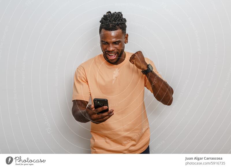 Man celebrating success while looking at smartphone in a light-colored top against a neutral background man african american celebration happiness joy victory