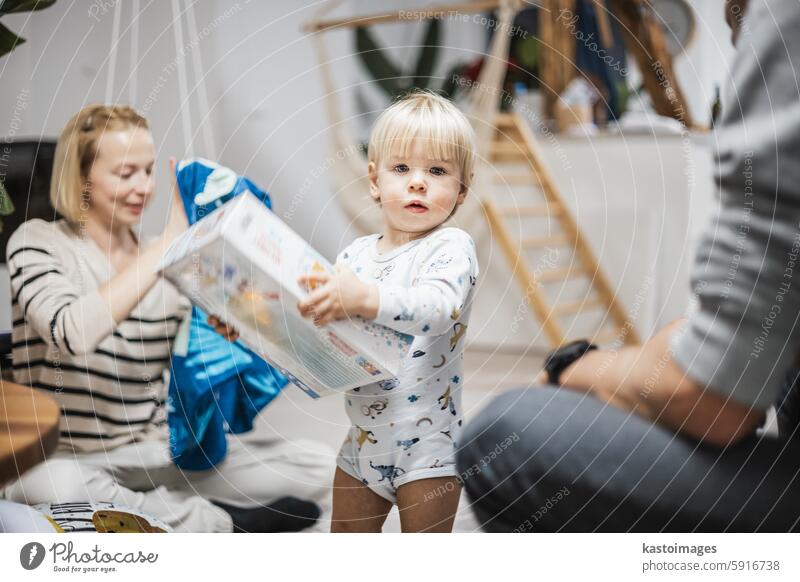 Cute little blond Caucasian toddler unpacking Christmas or Birthday present. Adorable small infant baby boy opening gift child celebration birthday room