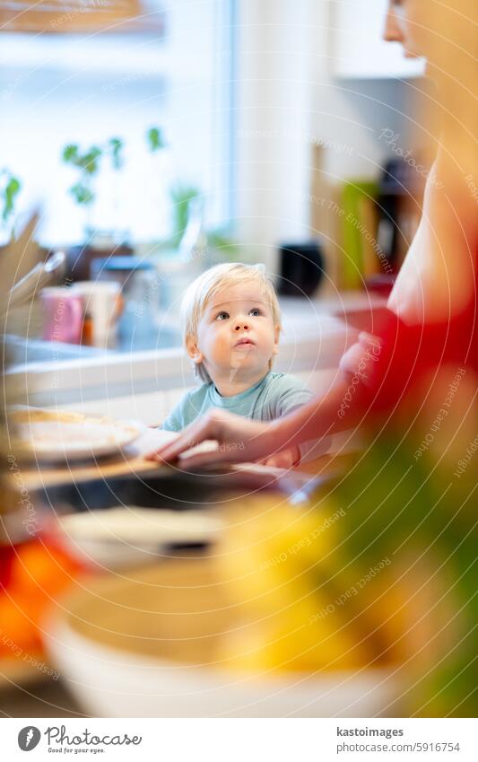 Mother and little toddler baby boy making pancakes for breakfast together in domestic kitchen. Family, lifestyle, domestic life, food, healthy eating and people concept.