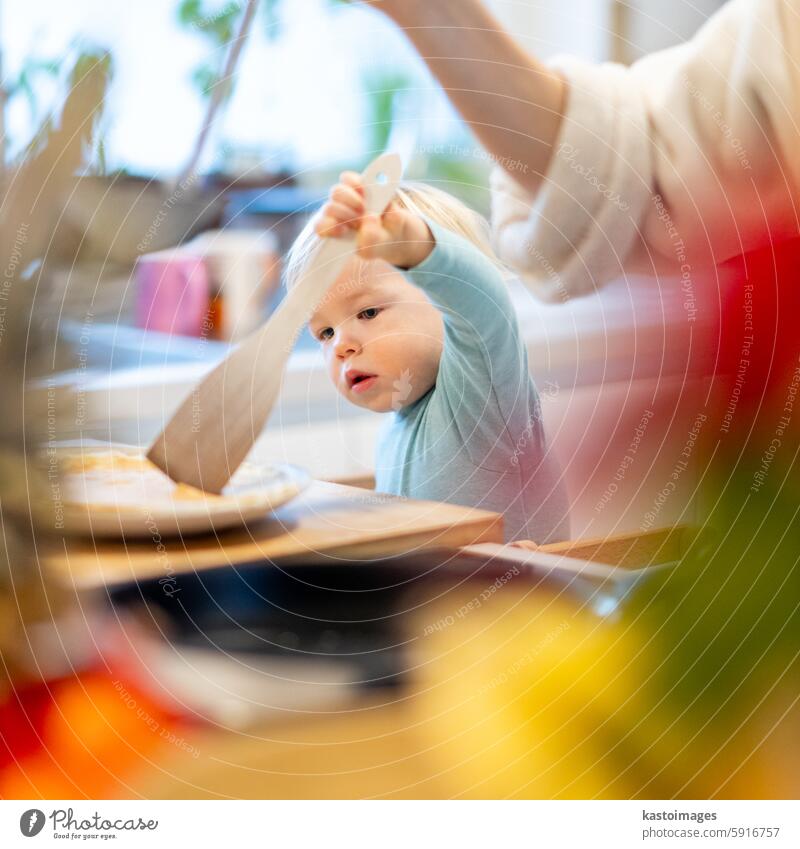 Mother and little toddler baby boy making pancakes for breakfast together in domestic kitchen. Family, lifestyle, domestic life, food, healthy eating and people concept.