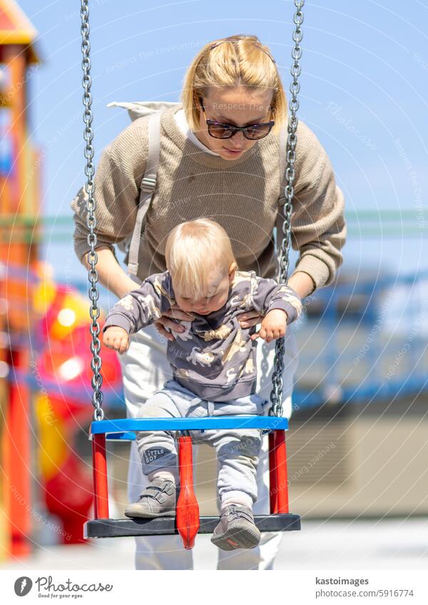 Mother pushing her infant baby boy child on a swing on playground outdoors. happy son family kid woman childrens playground childhood mother joy female toddler