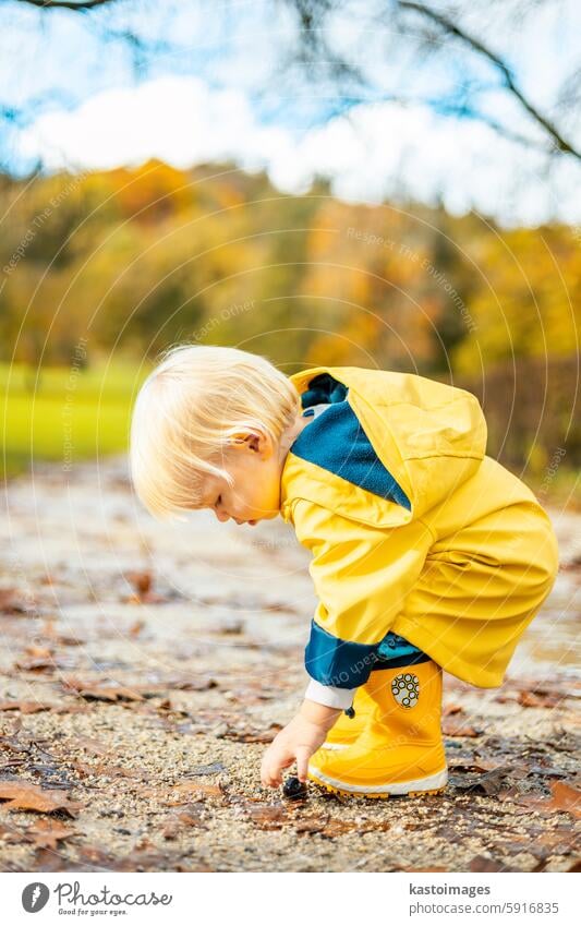 Sun always shines after the rain. Small bond infant boy wearing yellow rubber boots and yellow waterproof raincoat walking in puddles in city park on sunny rainy day.