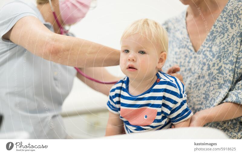 Infant baby boy child being examined by his pediatrician doctor during a standard medical checkup in presence and comfort of his mother. National public health and childs care care koncept.