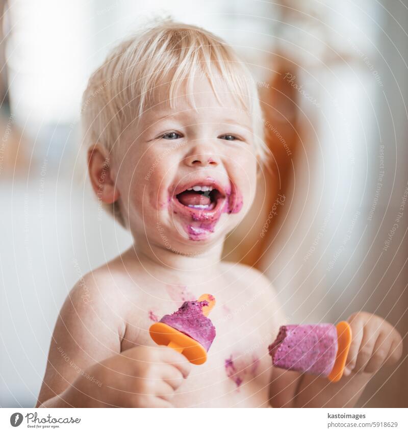 Happy adorable infant baby boy child smiling while eating two frozen fruit popsicle ice creams in simmer. kid food summer fun childhood snack little cute