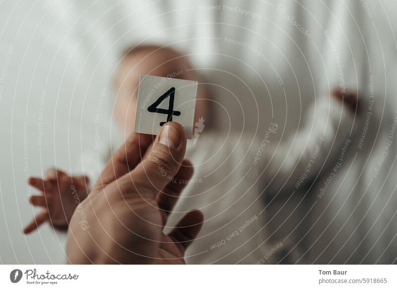 Dice with the number 4 in her hand, a baby blurred in the background Growth wax Baby Jubilee human hand cubes figures Digits and numbers Happy Colour photo