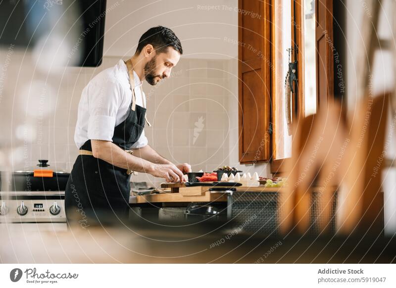 Private chef preparing meal in home kitchen professional male cooking slicing vegetables cutting board focused looking down modern well-lit domestic culinary