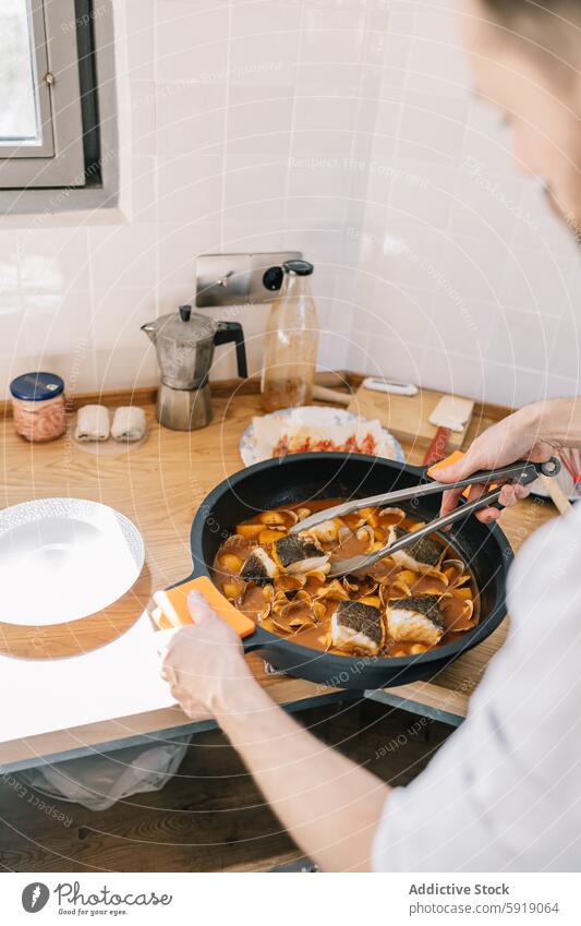 Private chef preparing fish dish in a cozy home kitchen cooking skillet man food private window indoor professional cuisine culinary gourmet seafood tongs