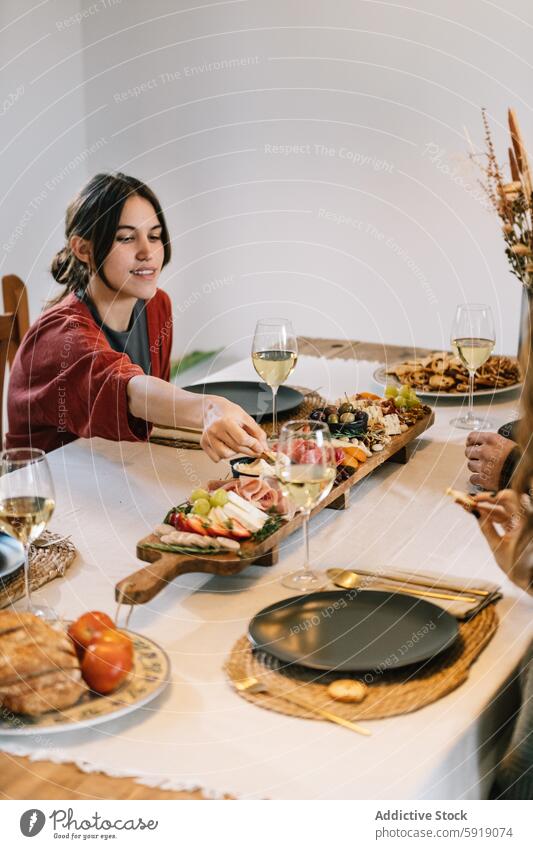 Woman serving food at cozy dinner party with friends woman wine glass charcuterie board table home casual engaging atmosphere reach dish variety communal