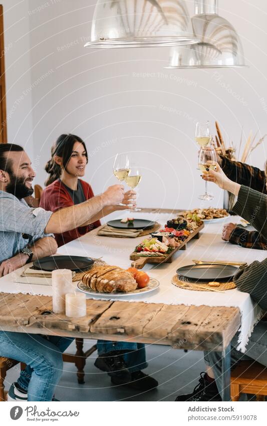 Friends enjoying a meal together with wine in a cozy home setting friends toast table rustic wooden cheerful man woman white wine dinner lunch togetherness