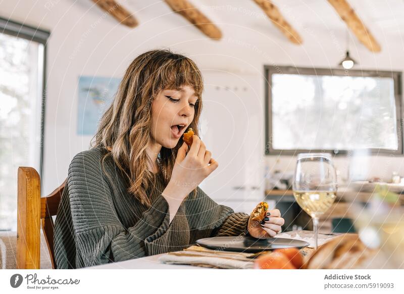 Woman enjoying a croquette at a stylish indoor dining setting woman home lifestyle enjoyment meal modern cozy table food savoring bright seated experience bite