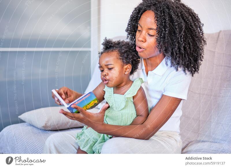 Mother teaching young daughter from a book on couch mother reading learning home indoor female child adult family woman girl bonding education african american