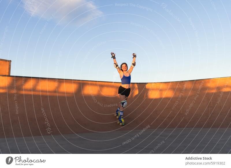 Young woman joyfully roller skating in a skate park young sunset victory arms raised wearing shorts tank top outdoor activity sport leisure recreation