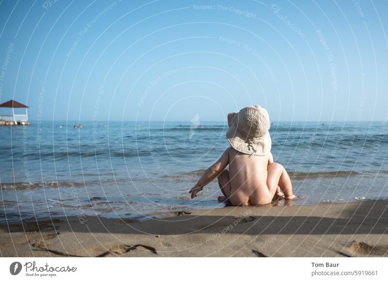 Baby with hat on the beach looking into the sea Child Cute Small pretty cute Caucasian White Soft Innocent Ocean Beach Far-off places Waves Sandy beach