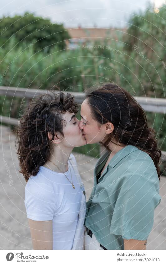 Lesbian couple kissing on bridge in daytime homosexual interact love relationship romance spend time trendy women lesbian soulmate romantic stand sneakers