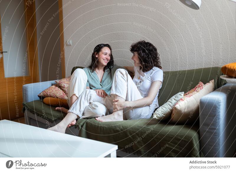 Smiling LGBT couple of women chilling on couch at home lesbian together lgbt sofa smile female love in love happy same sex cheerful sit bonding weekend