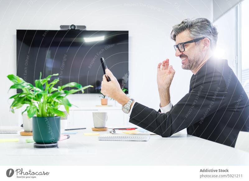 A joyful executive engages in a lively video call, waving to the screen, showcasing connectivity and modern work culture office business man suit technology