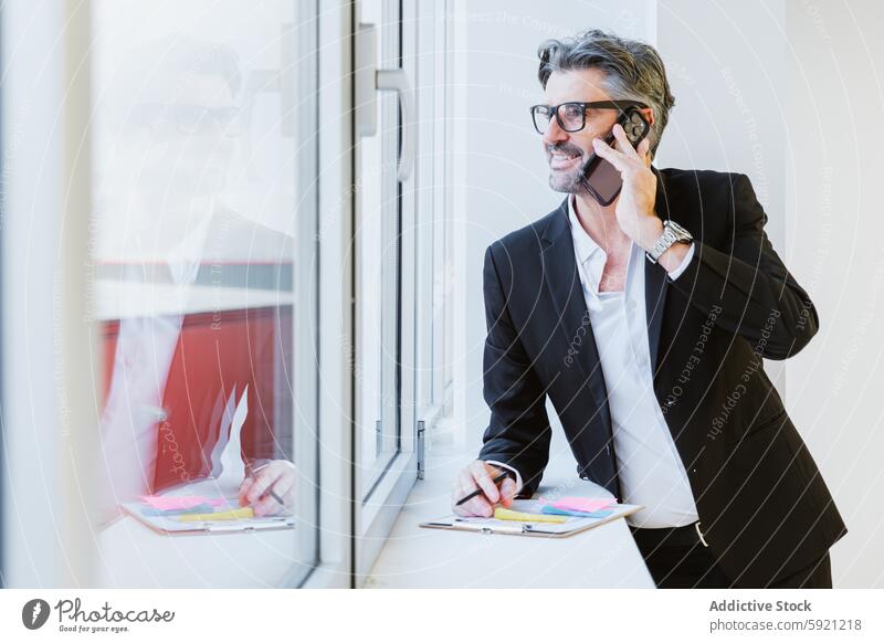 A stylish executive in conversation on his phone, with a cityscape reflected in the window, symbolizing connected business call reflection smile man style