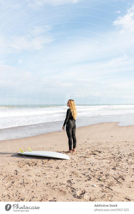 Young woman standing near surfboard on beach coast shore seashore hobby activity pastime sport cheerful happy water tide wave smile waterfront sand seaside