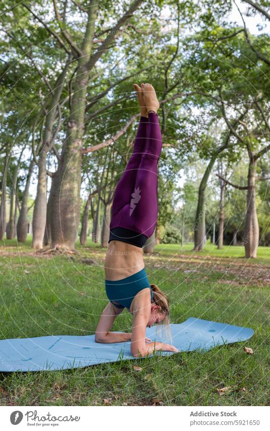 Slim female doing Eagle Legs position in Headstand pose in green park woman yoga eagle legs in headstand practice asana flexible balance vitality harmony