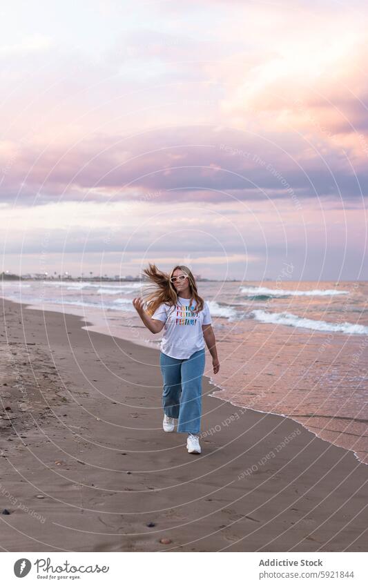 Content stylish woman walking on beach in sunset style young trendy summer positive sea sunglasses seaside female happy cheerful confident seashore coast