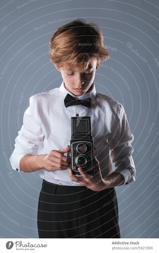 Preteen boy in white shirt and bow tie holding vintage photo camera digital device kid style preteen outfit fashion modern photography childhood apparel wear