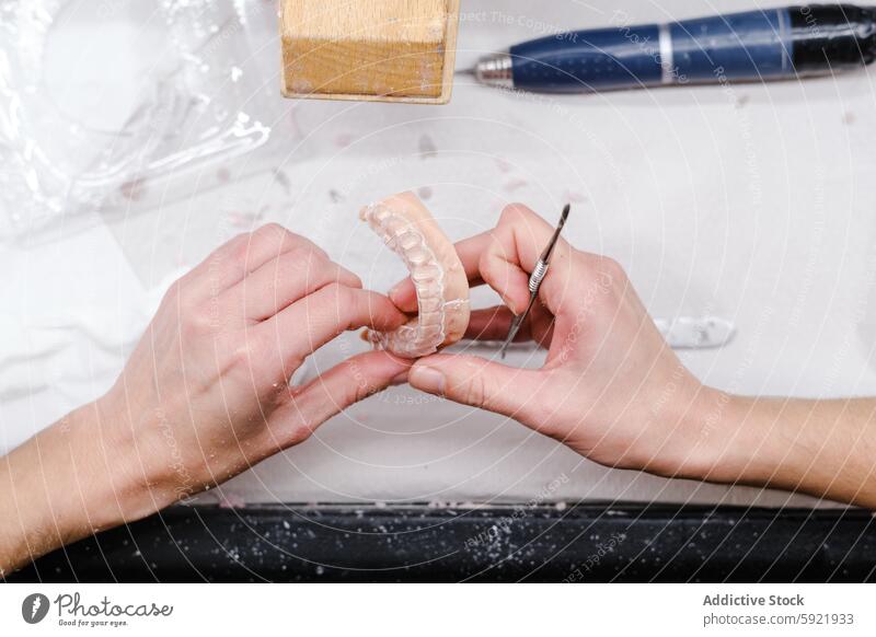 Dental technician artistically adjusts a dental mold hands adjustment tool workbench precision crafting prosthetic dentistry detail manual close-up