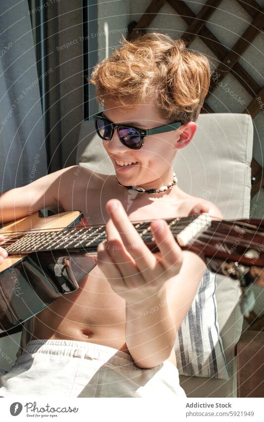 Young Boy Enjoying Music Playing Guitar Outdoors boy guitar playing music young sunglasses outdoor sunny day relaxation passion musical instrument leisure